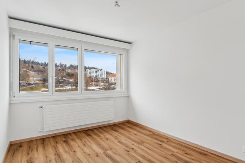 Empty room with white walls, wooden floor, large window with city view