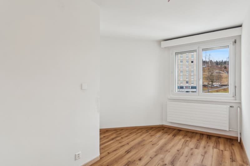 empty room with large window, wooden floor, white walls, radiator