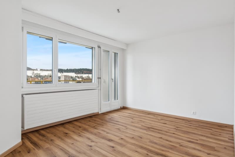 Empty room with large windows, hardwood floors, white walls, a heater and view of the city