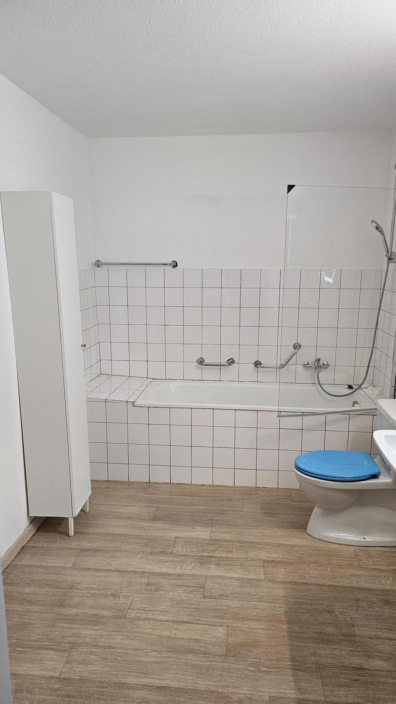 Bathroom with toilet, bathtub, and sink, wooden floor, white walls, white cabinet