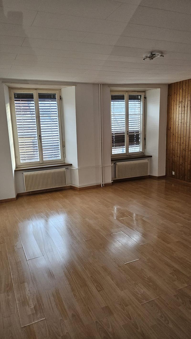 large open room, hardwood floors, two windows with white blinds, two white radiators