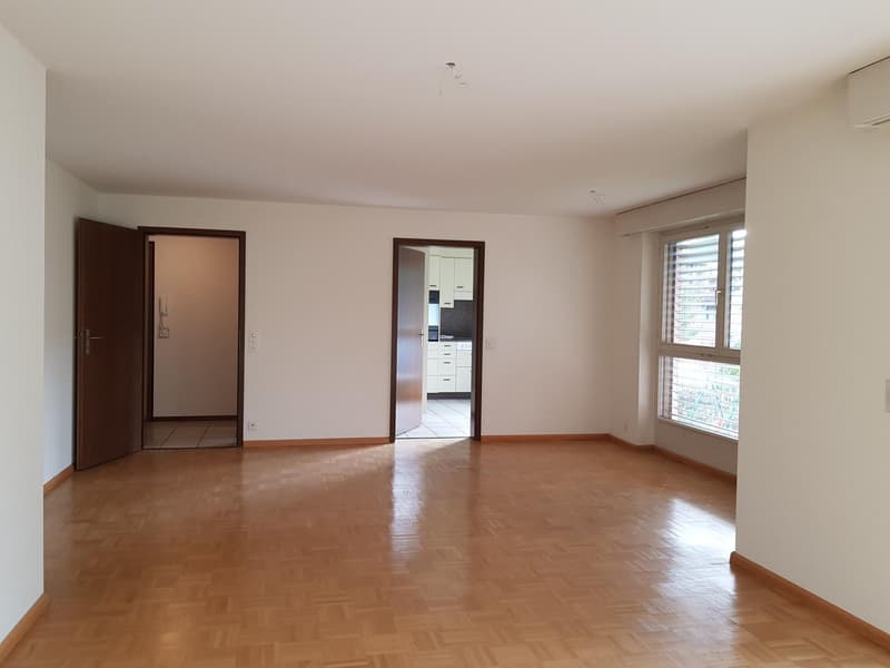Empty room with wooden floors, white walls, open doors, windows, and kitchen with drawers.