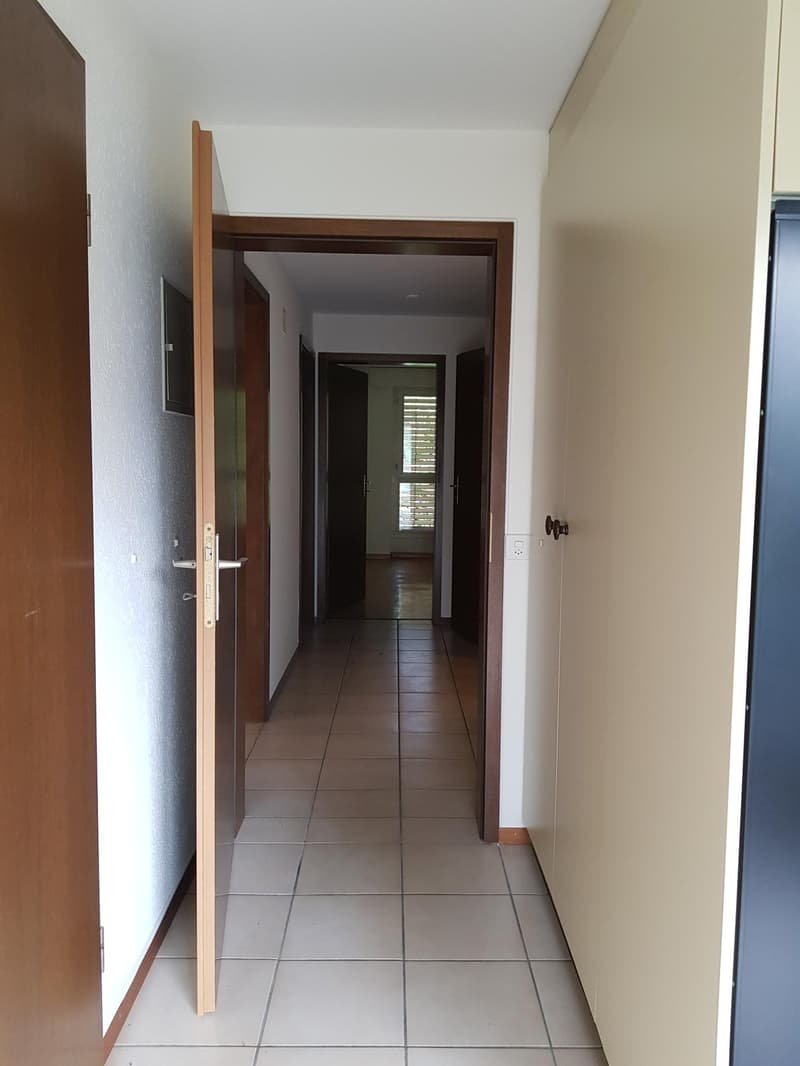 Tiled hallway with doors leading to different rooms, one of which has windows with blinds.