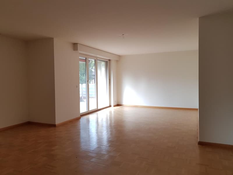 large empty room, hardwood floors, sliding glass doors leading to a balcony, white walls, natural light
