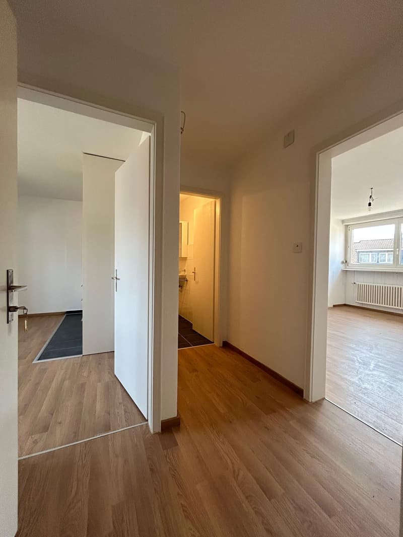 Empty room with wooden floors, white walls, open doors, and a window with a view of the outside.