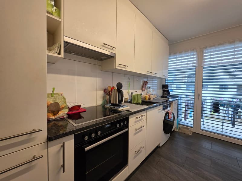 modern kitchen with white cabinets, black countertops, black stove, dishwasher, washing machine, large windows