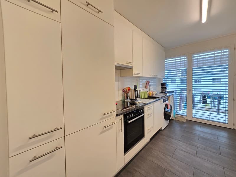 modern kitchen with white cabinets, wooden floor, black appliances, washing machine, dishwasher, large windows