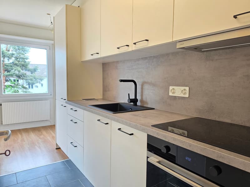 modern kitchen with white cabinets, gray countertops, black sink, black faucet, built-in oven, induction stove, and a window with a view of trees