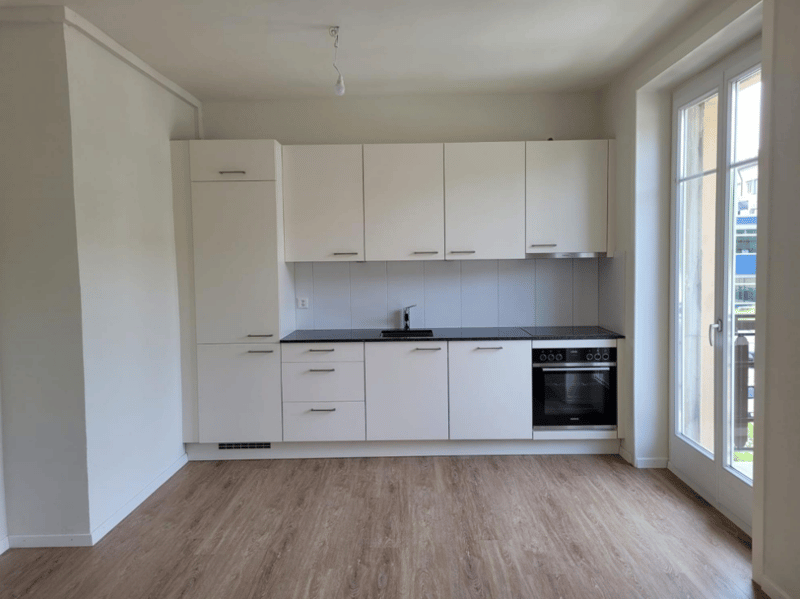 Spacious kitchen with white cabinets, black countertop, built-in oven, and hardwood flooring. Large window providing natural light.
