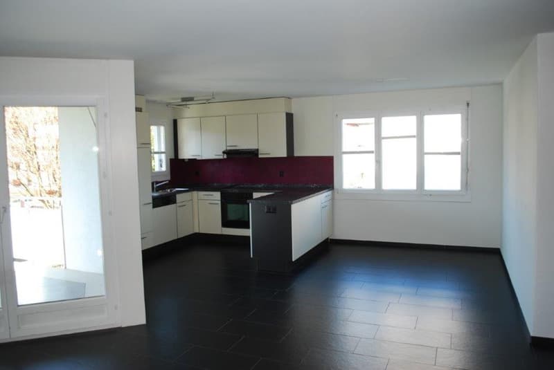 Modern kitchen with white cabinetry, black tiled floor, large windows, and a glass door leading to a balcony.