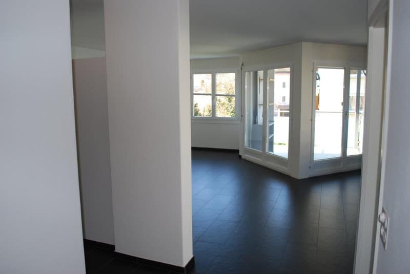 corner room with sliding glass doors to balcony, white walls, black tiled floor, panoramic window