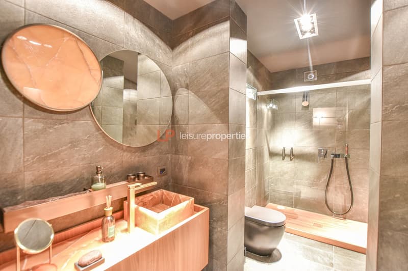 marble tiles, modern vanity, round mirror, walk-in shower, floating toilet, floor-mounted faucet