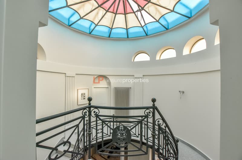 spiral staircase with decorative iron railings, central blue stained glass dome, white walls