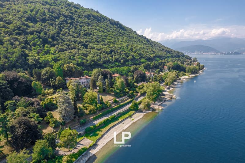 Villa on hillside, near a shoreline, surrounded by greenery, mountains and a lake in the background