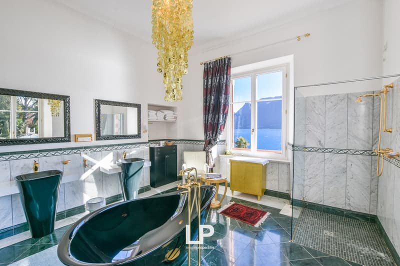 green tiled floor, glass shower, bathtub, two sinks, mirror, window with view, chandelier
