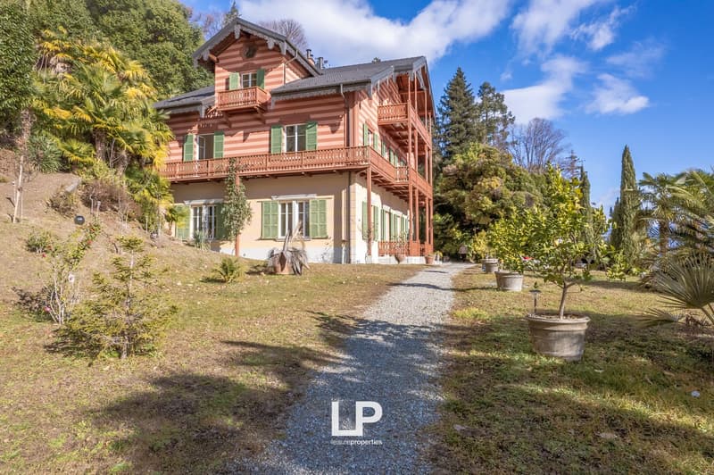 large house with balconies, red and white striped wall, green windows, gravel driveway, trees