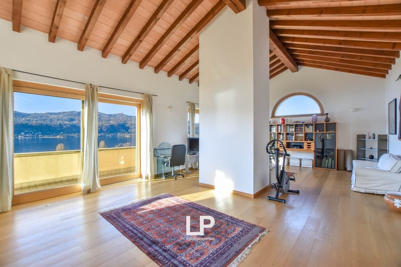 Spacious living room with large windows offering a scenic view of the lake, wooden beamed ceiling, hardwood floors, area rug, home office setup, and bookshelves