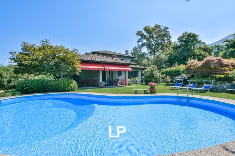 green lawn, trees, swimming pool, house with red awning, bench, chairs, flowers