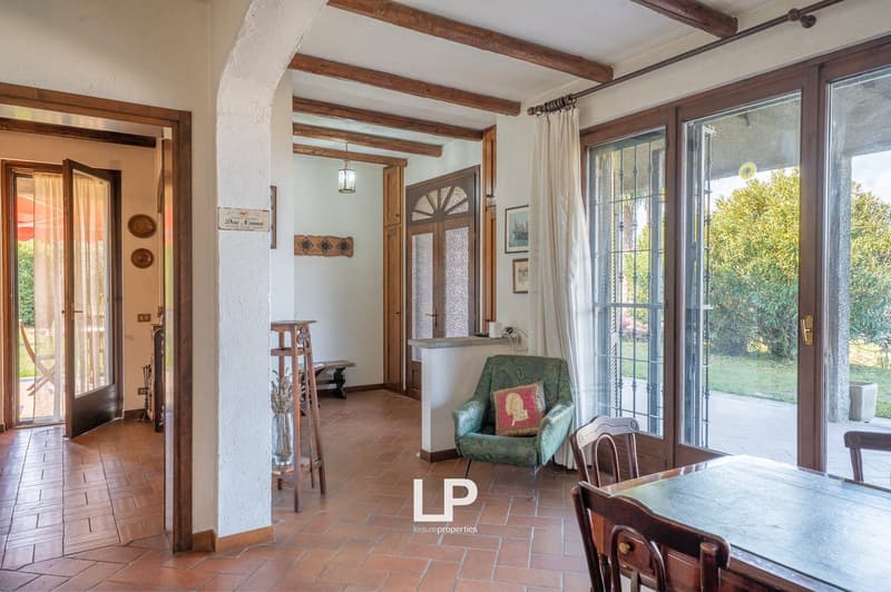 open living room with dining area, wooden floor, large windows, wooden furniture, green armchair, table, chairs