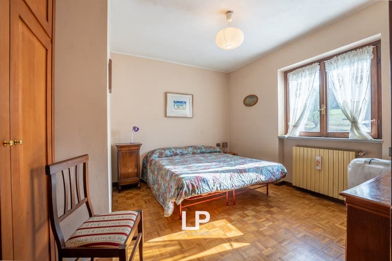 Bedroom with bed, wooden cabinet, chair, lamp, picture frame, radiator, window with curtains