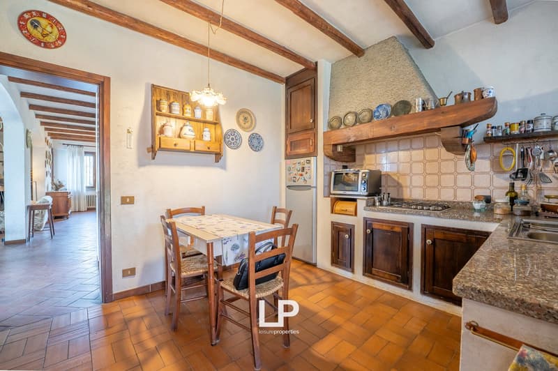 Dining room with wooden table and chairs, kitchen with appliances, wooden shelves, tiled floor, decorative plates, clock, and fireplace