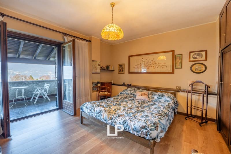 bedroom with bed, balcony with table and chairs, wooden floor, wall paintings, lamp