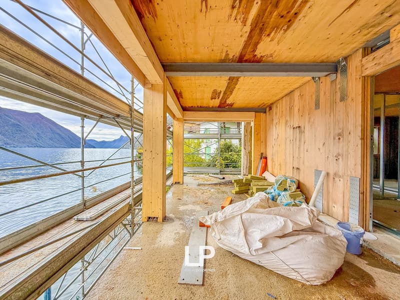 Under construction balcony, with unfinished wood walls, overlooking a lake and mountains, with glass walls and metal frames, various materials and tools are around