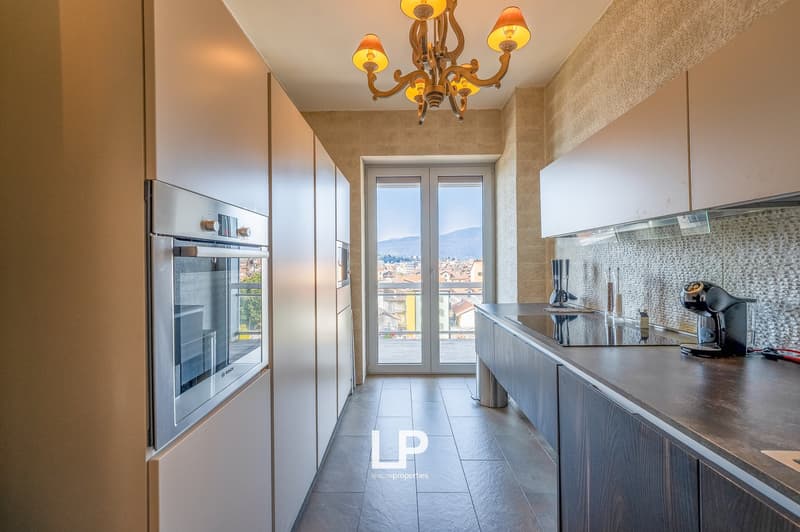 Spacious kitchen with large windows offering a scenic view, modern appliances including a refrigerator and coffee maker, tiled flooring, and a chandelier lighting fixture.