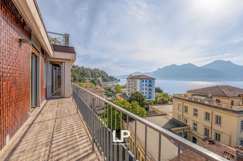 Brick building with balcony, overlooking a lakeside town with mountains in the background