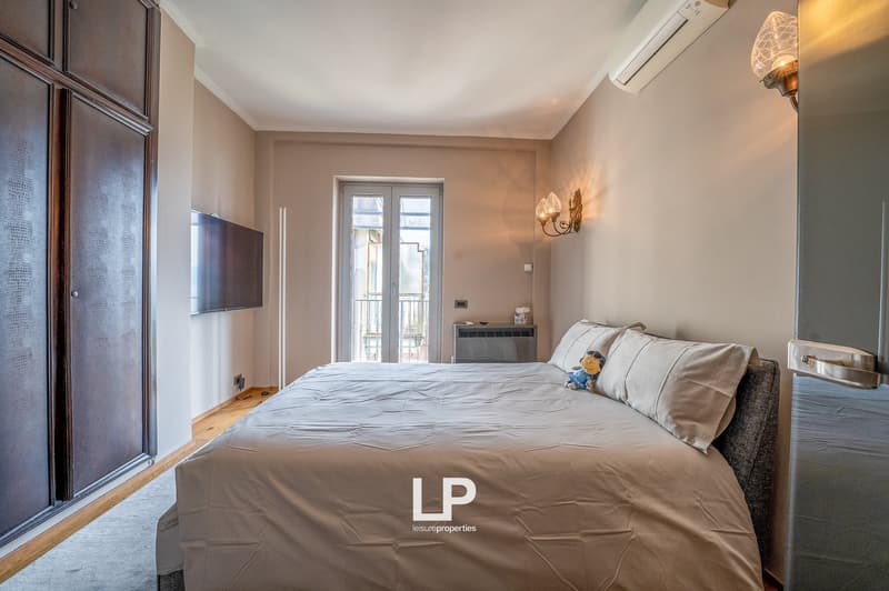Spacious bedroom with large windows, wooden flooring, a king-size bed, a TV mounted on the wall, and a balcony or terrace access.