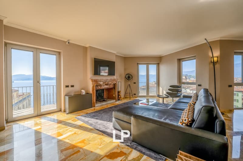 Spacious living room with large windows, balcony, fireplace, leather sofa, and modern decor