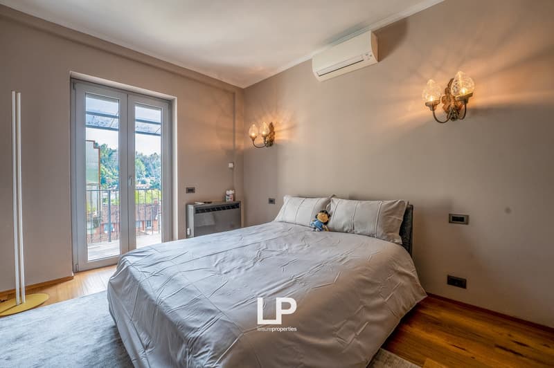 Spacious bedroom with large windows, hardwood floor, gray bedding, wall-mounted air conditioning unit, and decorative wall sconces.
