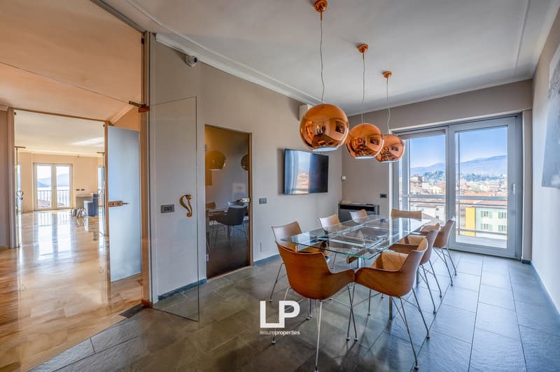 Spacious open-plan living area with glass dining table and chairs, copper pendant lights, large windows with city view, sliding glass doors leading to a balcony or terrace