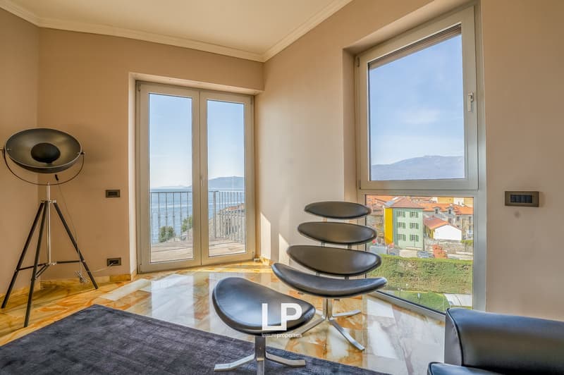 Spacious living room with large windows offering a scenic view, marble flooring, modern black leather seating, and a tripod lamp
