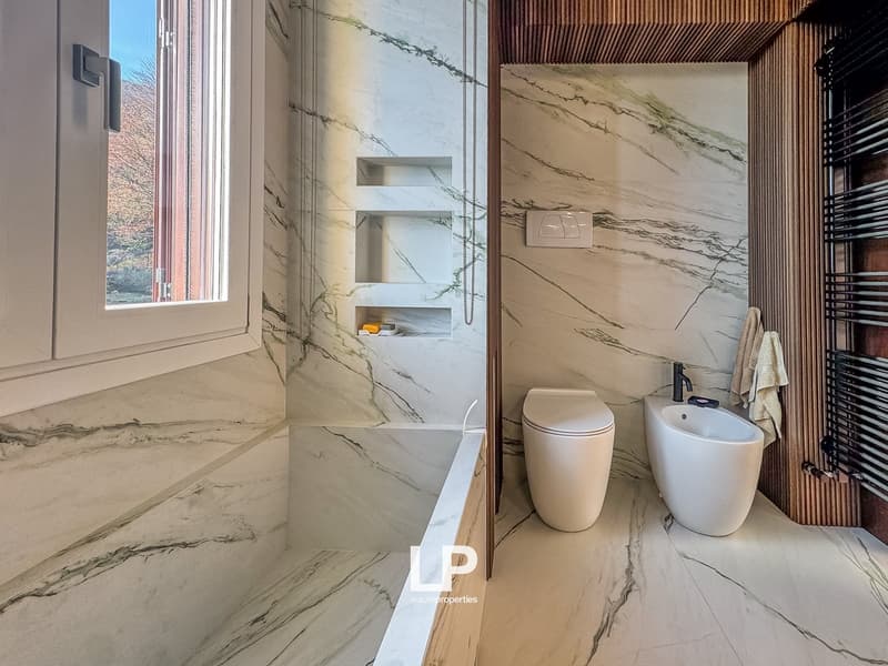 modern bathroom with marble walls, bathtub, toilet, bidet, shelves, window