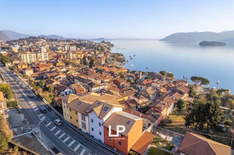 Row of residential buildings along the coastline, varied building sizes and styles, cars driving on a road, lake view