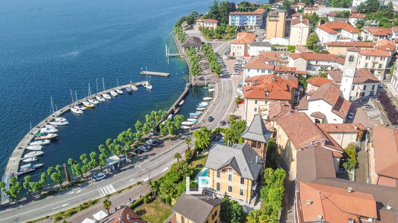 Aerial view of a coastal town with buildings, boats docked at a marina, a road with cars, greenery, and a waterfront