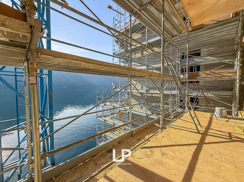 Under construction building with steel scaffolding, wooden planks on balcony, and a stunning lake view