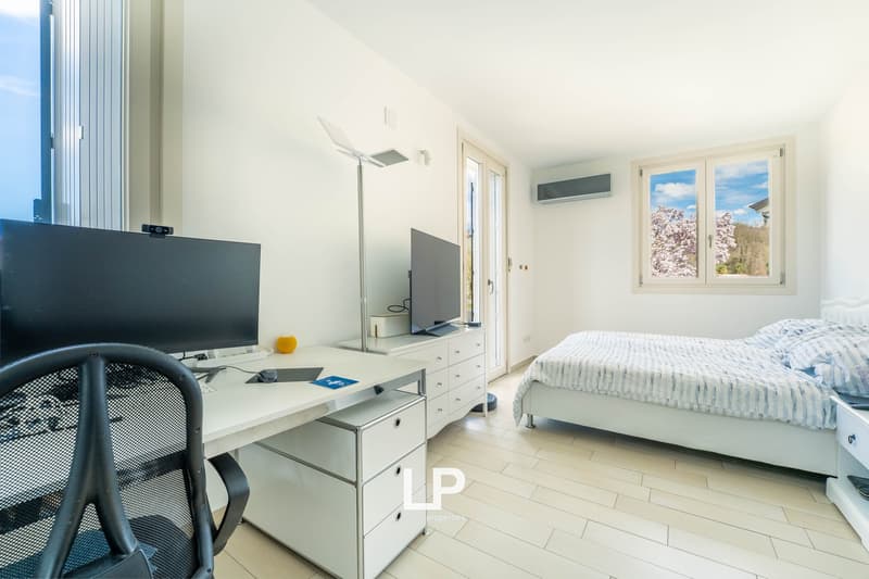 Single bed with white headboard, large desk with computer, office chair, two windows, hardwood floors