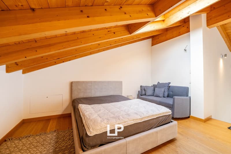 bedroom with bed, couch, carpet, wooden floors, white walls, exposed wooden beams
