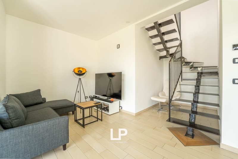 White walls, gray sofa, TV, table, orange lamp, white chair, metal staircase