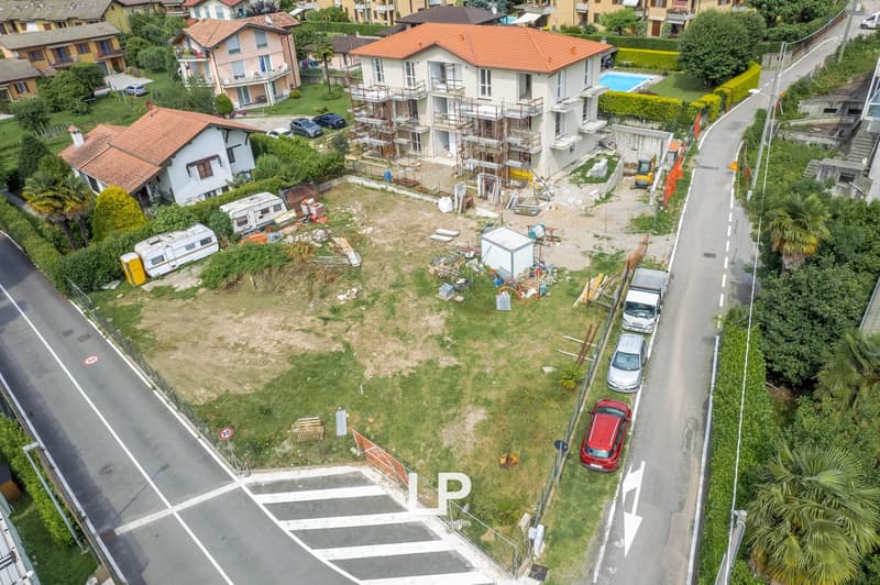 Aerial view of a residential area with ongoing construction work. The image shows several multi-story apartment buildings, some of which are under renovation or construction. There are also some smaller houses, a parking area, and various construction mat