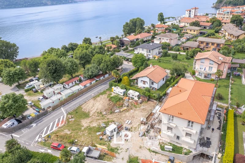 The image shows an aerial view of a residential area along a lake or river. The area is characterized by a mix of multi-story buildings, single-family homes, and some construction or renovation work visible in the foreground. The buildings have red tile r
