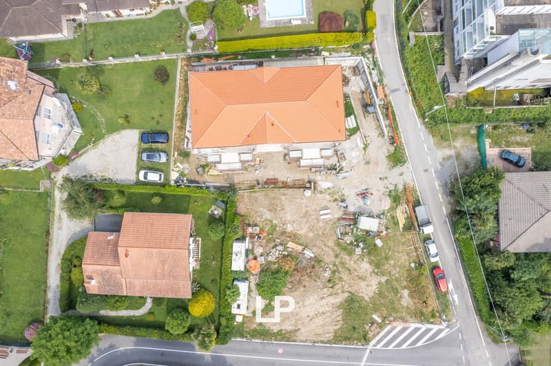 Aerial view of a residential property with a large house, a garden, and a parking area. The house has a red tile roof and is surrounded by greenery. There appears to be construction or renovation work taking place on the property.