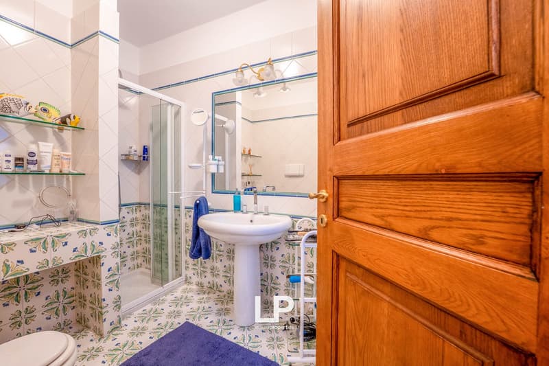 Tiled bathroom with floral pattern, pedestal sink, glass shower enclosure, wooden door frame