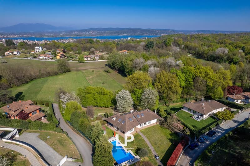 Spacious residential area with several houses, one with pool, surrounded by greenery and mountains in the background