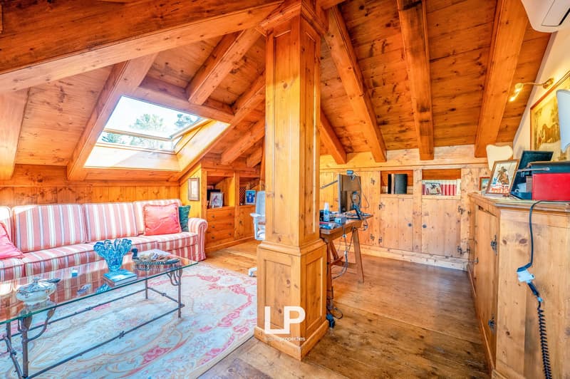 Cozy living room with wooden beamed ceiling, large windows, striped sofa, coffee table, and shelving units