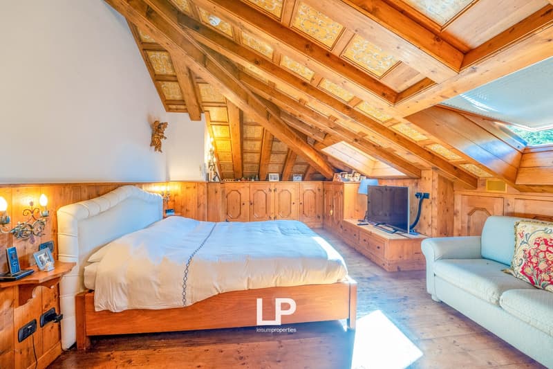 Spacious bedroom with wooden beamed ceiling, wooden furniture including a large bed and cabinets, and a cozy seating area with a sofa.