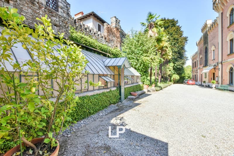 Stone building with green ivy and vegetation, metal-roofed structure, palm trees, gravel pathway, LP property sign