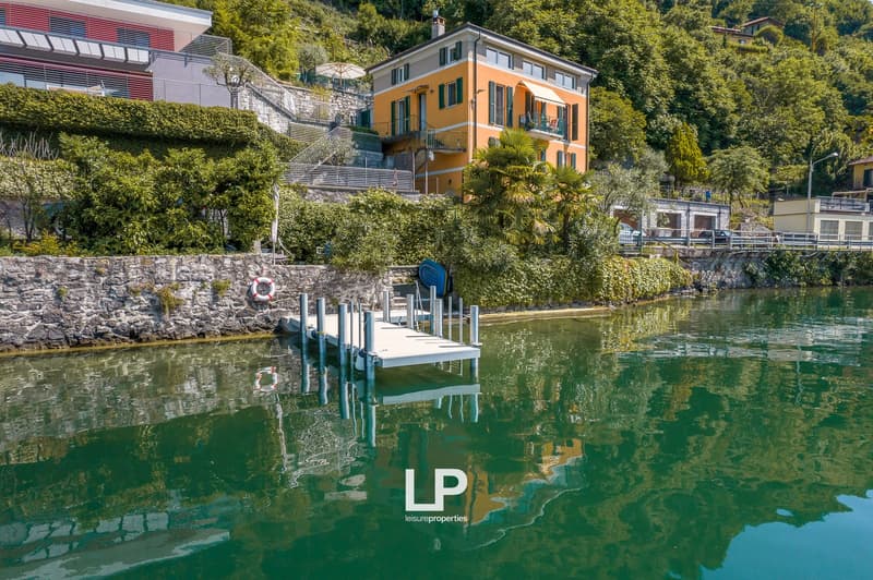 3-story orange building with balconies, surrounded by lush greenery and located on the waterfront with a dock and boats